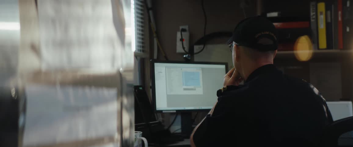 Uniformed man working on a desktop computer in a room lit by sunlight