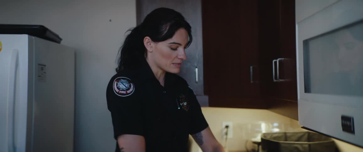 Woman dressed in fireman uniform cutting vegetables and cooking while talking and smiling on a kitchen indoors