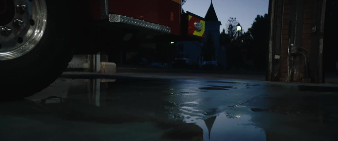 Person using a squeegee to clean the wet floor beside a fire truck at dusk