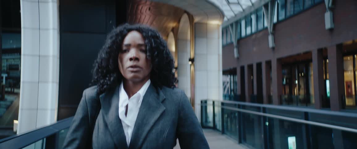 Woman in a suit adjusting her collar while walking through a lit urban corridor