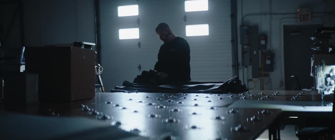 A man works alone in a garage surrounded by tools and equipment