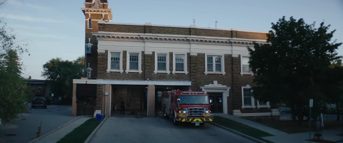 A fire truck drives out from a fire service department building at sunrise its lights catching the early morning glow as it heads into the quiet streets