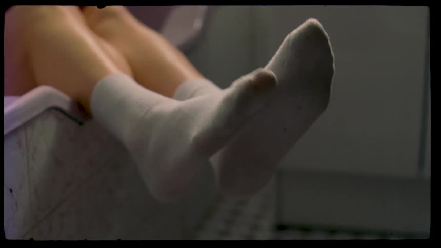 The video clip is a closeup lowangle shot of a persons legs and feet wearing light grey or white socks the feet are propped up on a surface with the persons movements suggesting a moment of relaxation