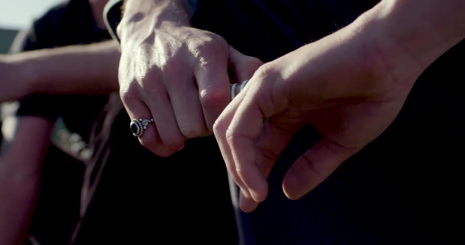 Hands close together holding a metallic object under sunlight