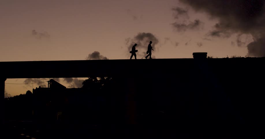 Two people walk on the overpass as the sun sets