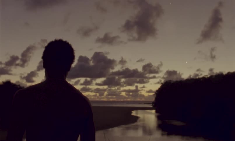 Person taking off their shirt in front of a river at sunset