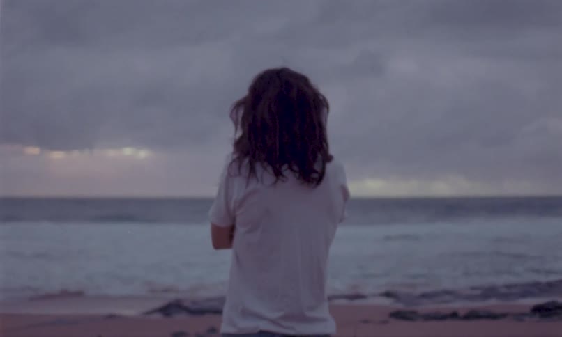 Person with long hair watches the sea at sunset