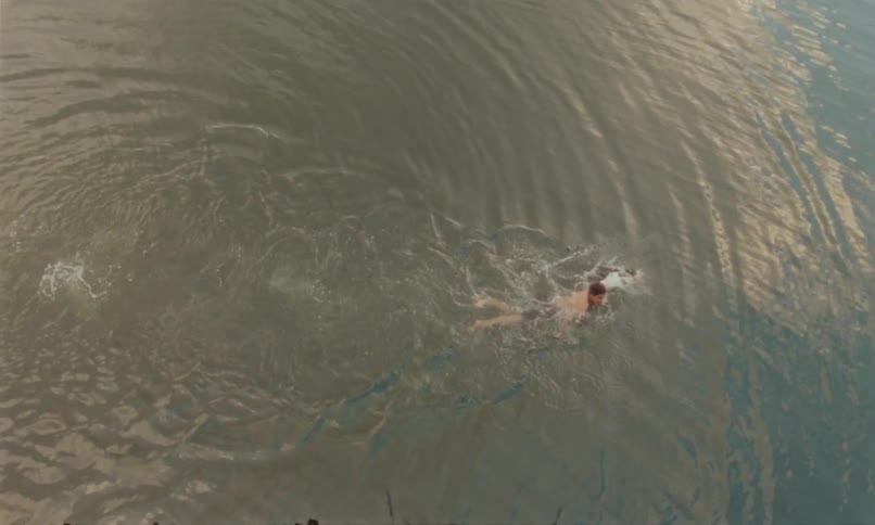 The video clip is an overhead view of a person swimming in a murky browntinted body of water the swimmer is performing a front crawl stroke creating small ripples as they move through the water