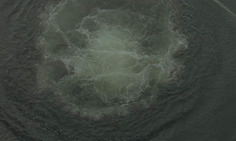 The video clip shows an overhead view of a large splash in a dark body of water as if something heavy has just dropped in the ripples and turbulence expand outwards from the point of impact before slowly subsiding