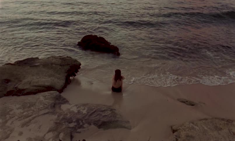 Person sitting by the sea between rocks at sunset