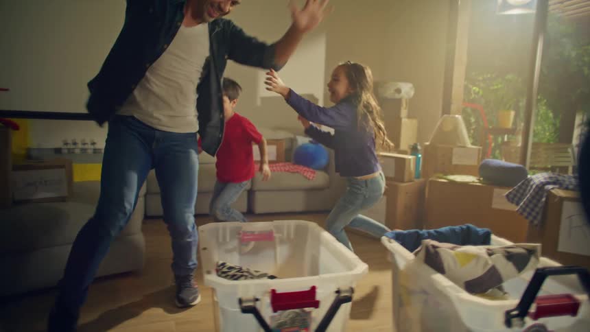 Family playing and dancing in a living room with moving boxes in the background
