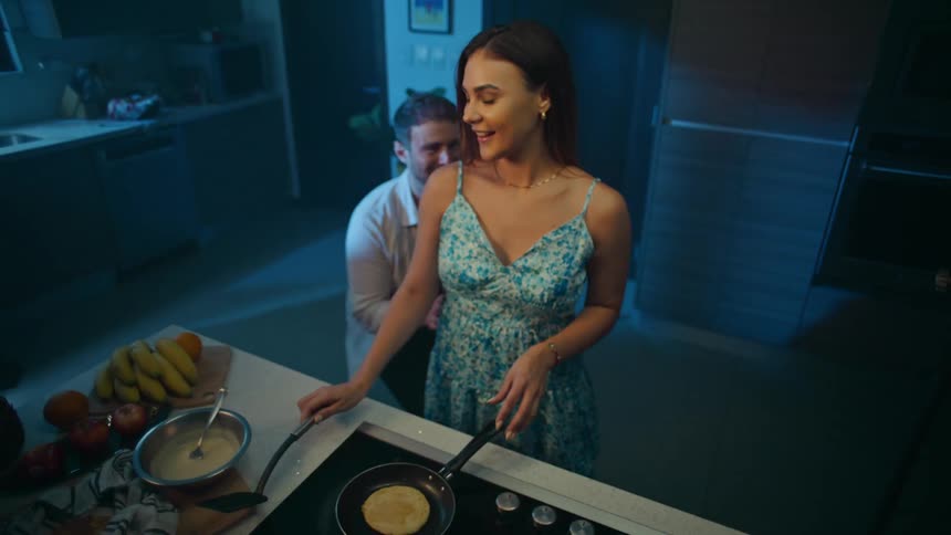 Couple laughing and hugging while making pancakes in the kitchen