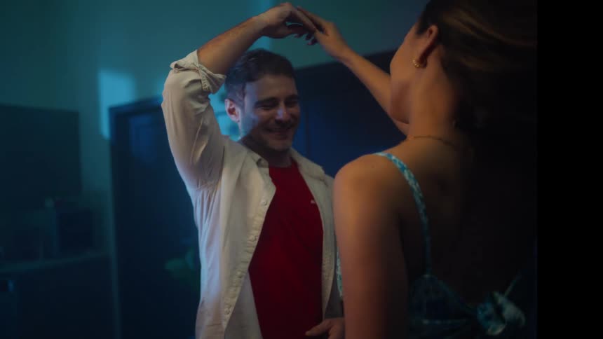 Couple dancing joyfully indoors under bluish lighting