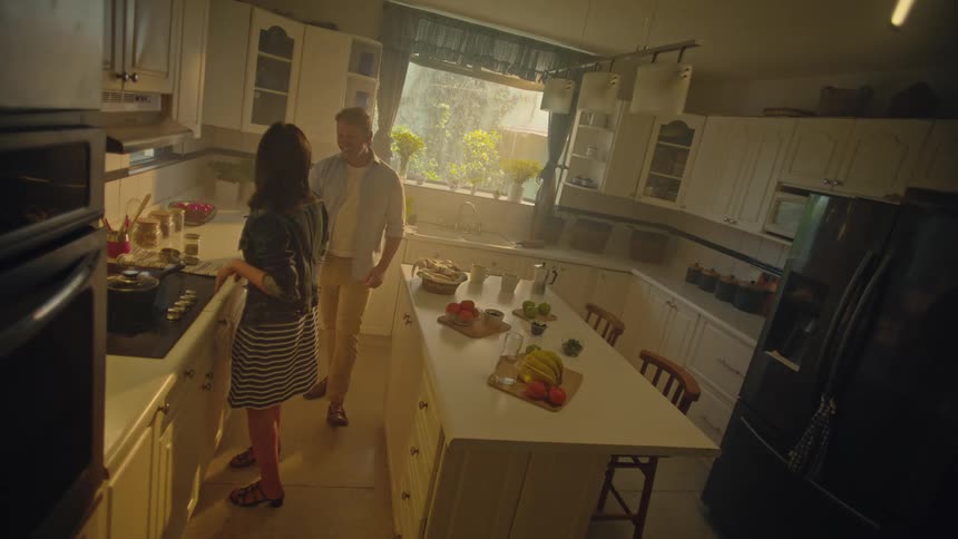 Couple dancing joyfully in the kitchen lit by the evening sunlight
