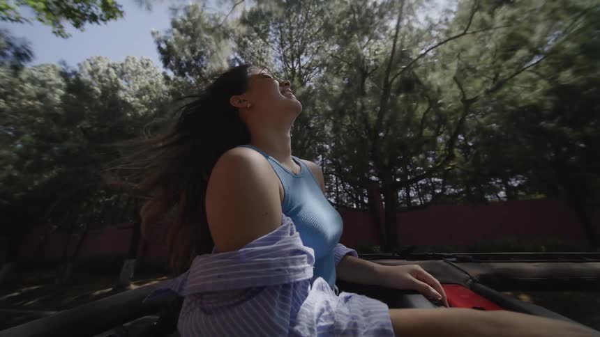 A young woman standing through a vehicles open roof while on a road trip during daytime