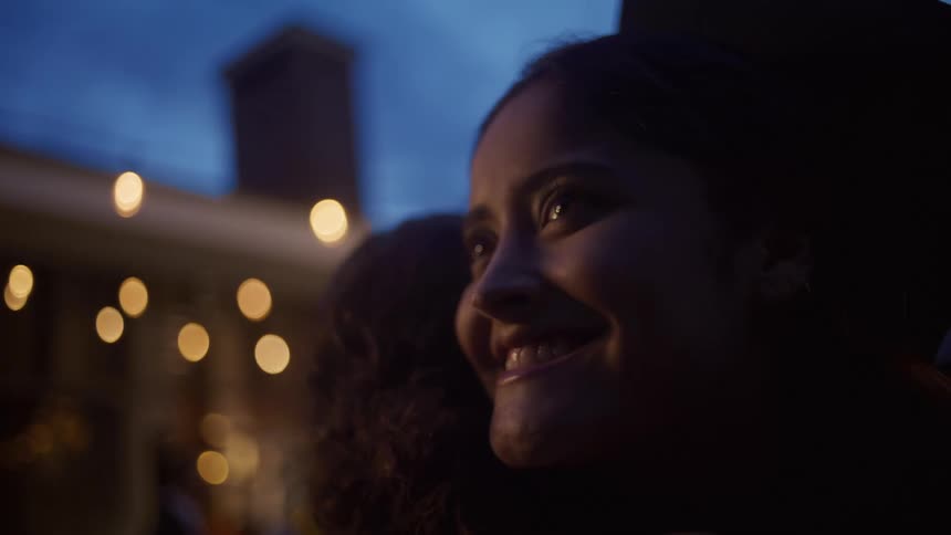 Woman smiles warmly while hugging another person outdoors in the evening