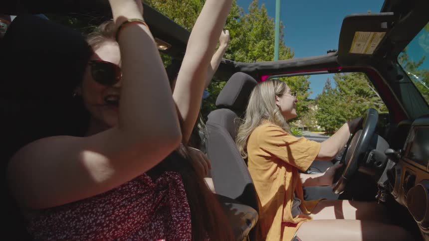A group of female friends celebrating in a car while on a road trip during daytime