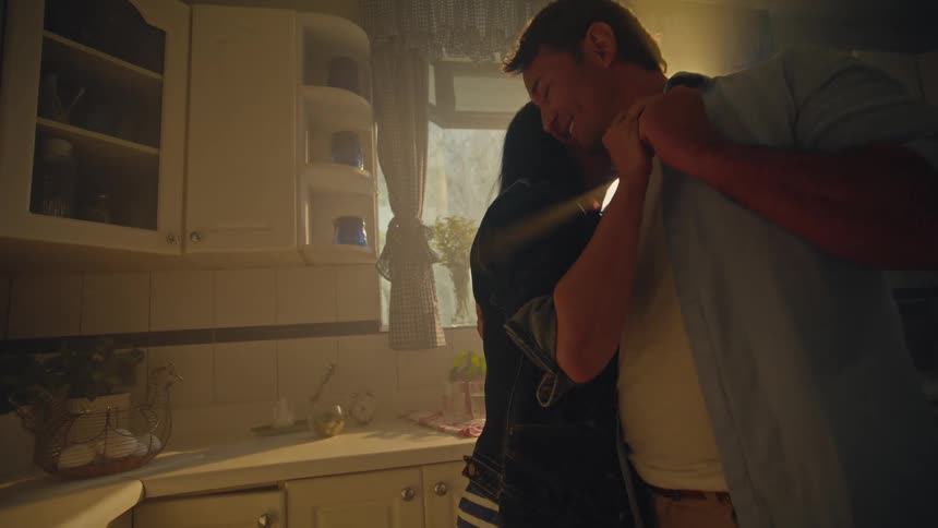 Couple kissing in a kitchen lit by the soft light of dawn