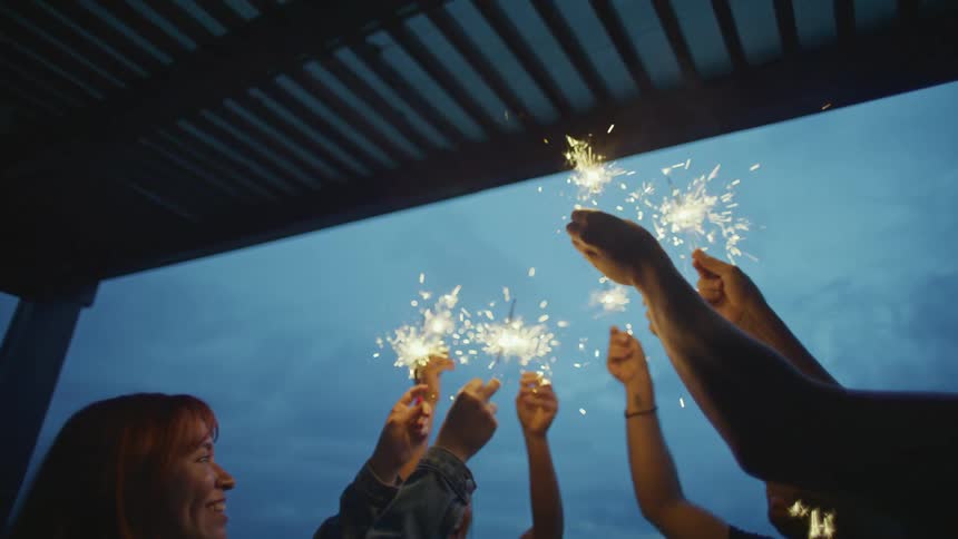 Group of people celebrating at night under a roof holding lit sparklers