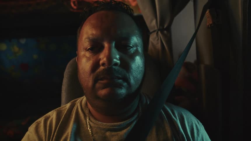 Man inside a truck at night wearing a seatbelt and lit by bluish and orange lights