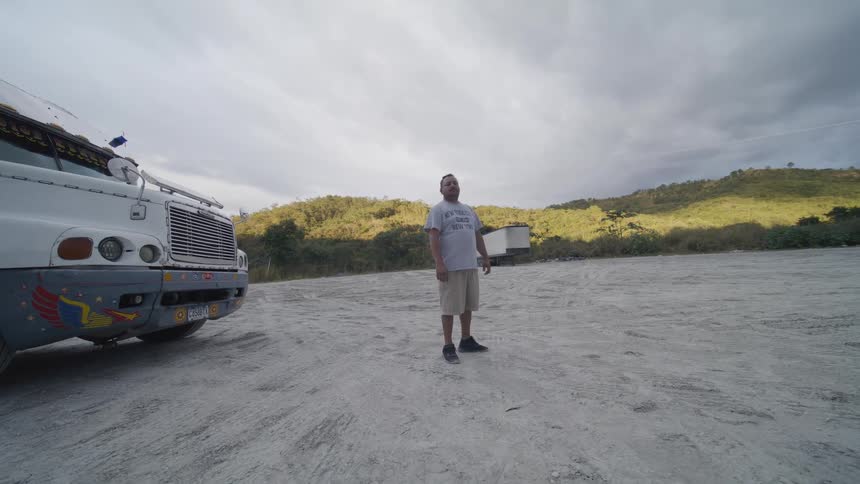Man standing next to a parked truck in an open area with hills in the background