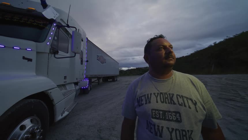 Close up of a hispanic man standing outdoors beside a cargo truck at dusk