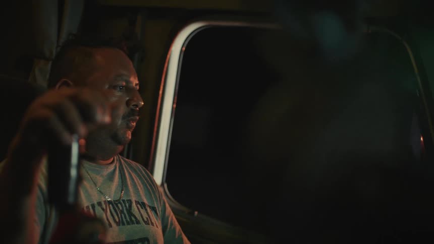 A middleaged man drives a truck through the night his hand gripping and shifting the massive gear as headlights cut through the darkness