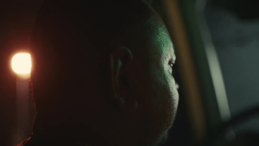Silhouetted by the passing city lights a man with a mustache drives a car at night