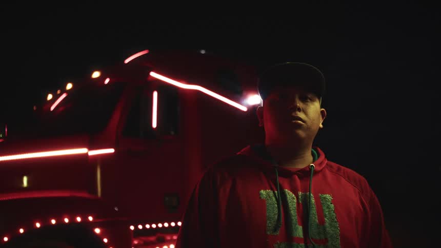 Man in a red hoodie standing in front of a truck lit by red lights at night