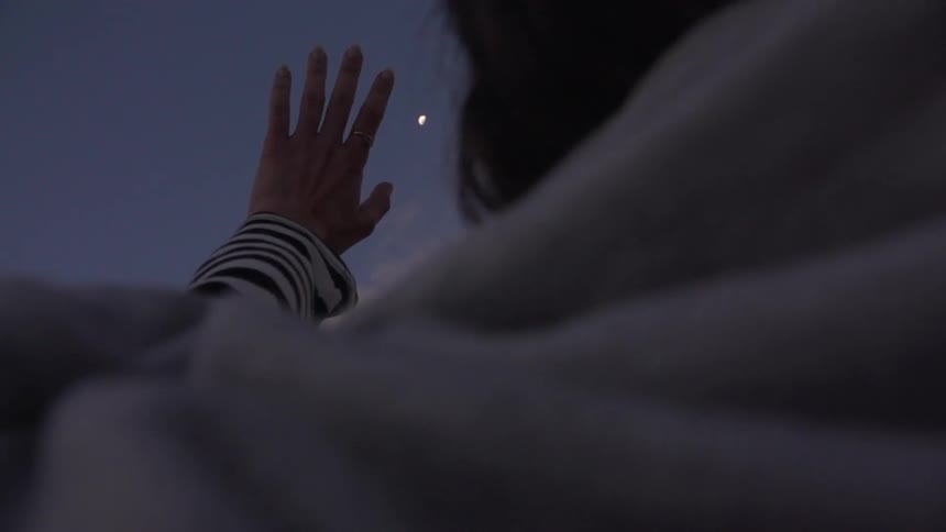 Person raises hand to a sunset sky