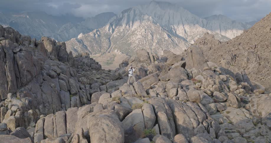 Aerial of a man viewing the environment with a pair of binoculars while standing outdoors on a rocky summit during daytime