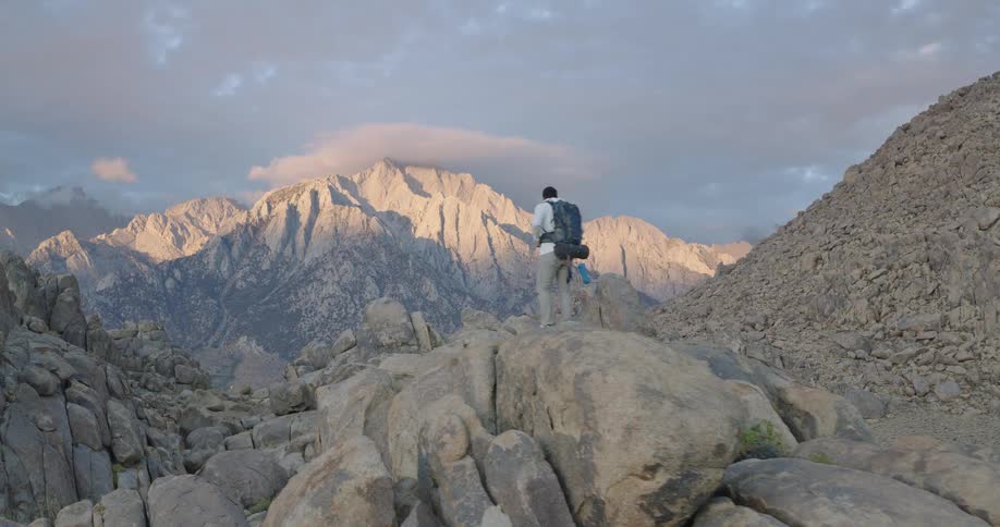 Bathed in warm sunrise light the hiker pauses on a rounded rock to take in glowing mountains ahead posture calm and contemplative