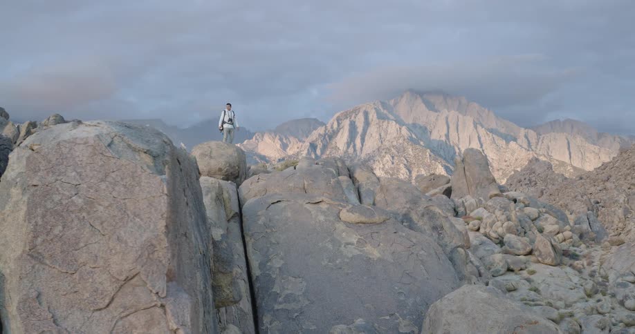 Male hiker stands on a boulder ina boulder field in mountainous terrain on a cloudy autumn day