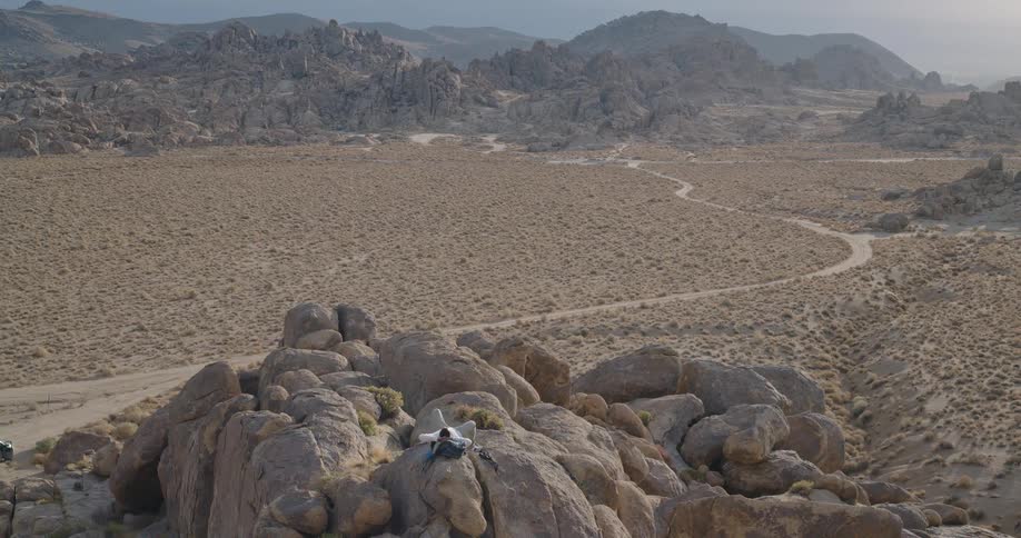 A lone hiker with a prosthetic leg relaxes on a rocky outcrop overlooking a vast arid landscape