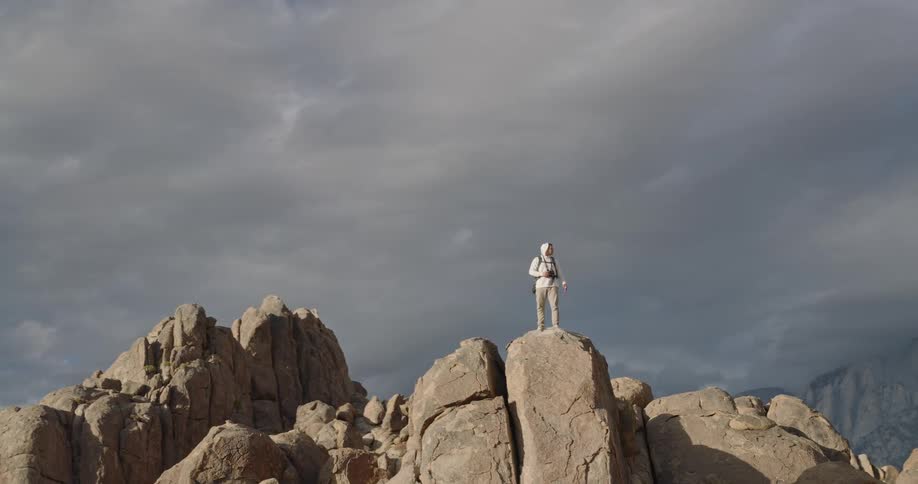 Hiker stands on a stone cliff in a mountain range under an overcast sky and looks at the scenery
