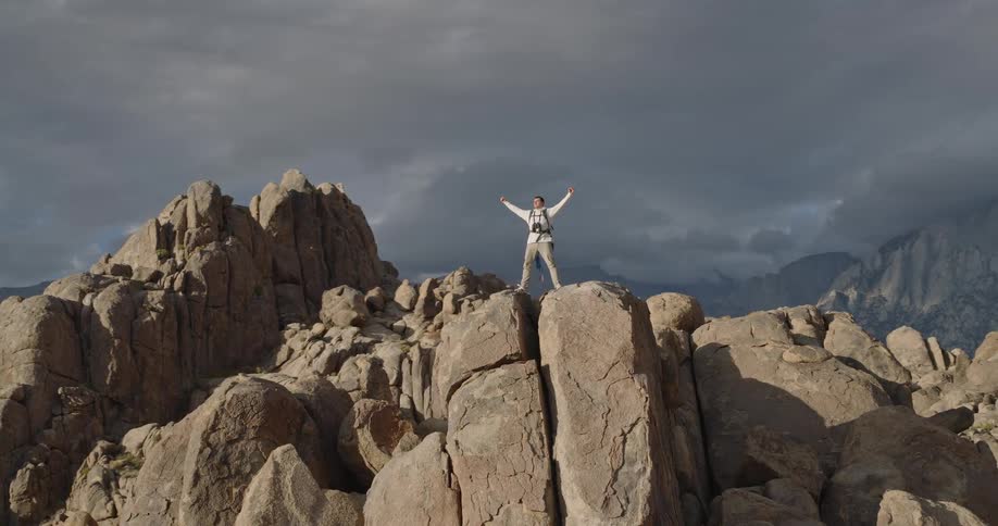 Aerial of a man celebrating while standing outdoors on a rocky summit during daytime