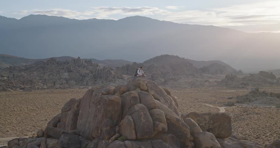 Male hiker sits at the top of a pile of boulders standing near a dirt roadin mountainous terrain on a foggy autumn day