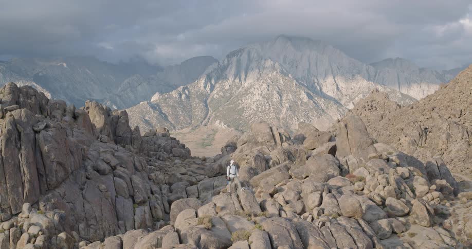 Aerial of a young man standing outdoors on a rocky summit in a desert during daytime
