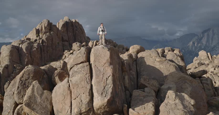 Person standing on rock formation in mountainous area under cloudy sky
