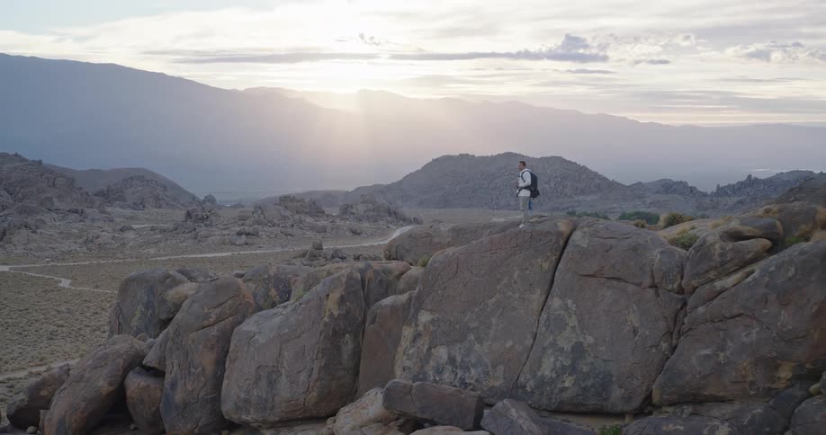 Soft sunrise rays spill over a wide desert basin of sage and rounded boulders with hazy mountains layered in the distance
