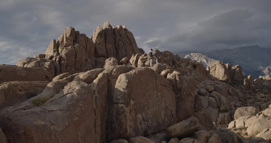 Aerial of a young man taking pictures with his phone while standing outdoors on a rocky summit during daytime