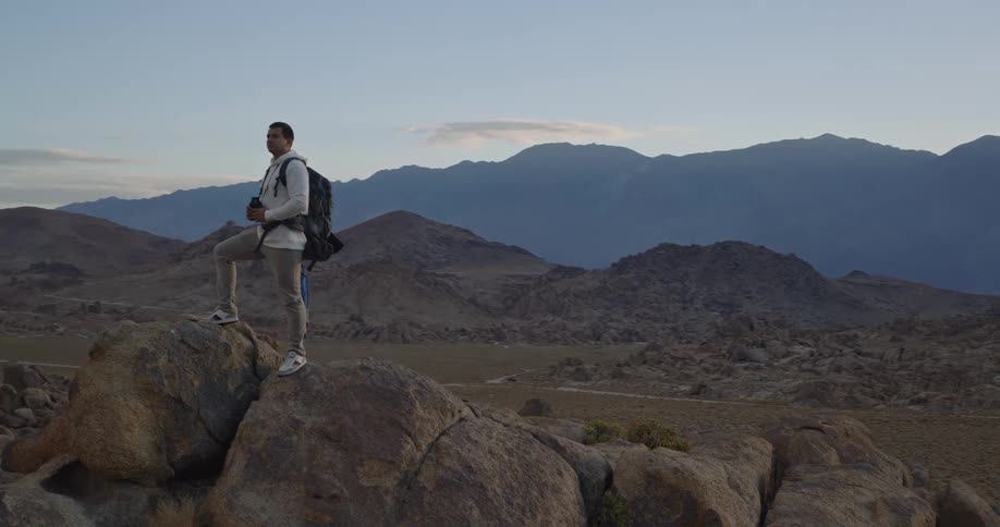 Man standing on rock formation in mountainous desert under clear sky