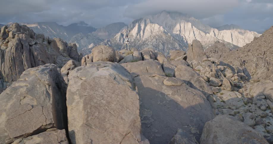 Rocky mountains with sunlit peaks and person walking among boulders