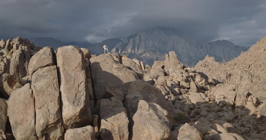 Person walking among rocks in mountainous terrain under cloudy sky
