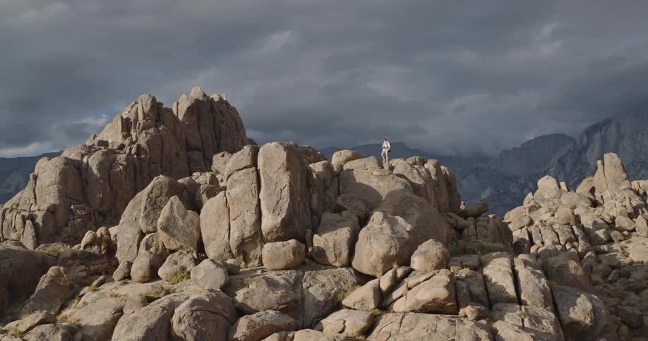 A person hikes along a mountain trail surrounded by large rocky formations under a cloudy sky the terrain rugged and dramatic as mist clings to the peaks