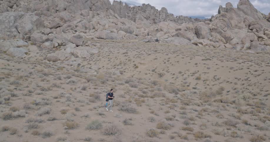 Man walking alone through desert landscape with dry vegetation and mountains in the background