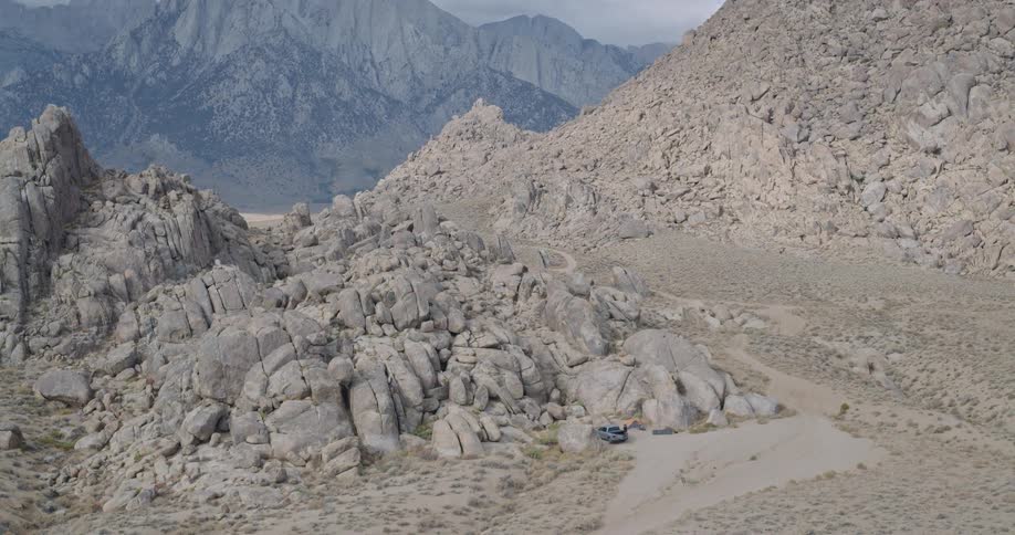 Vehicle on dirt road surrounded by rock formations and mountains in the background