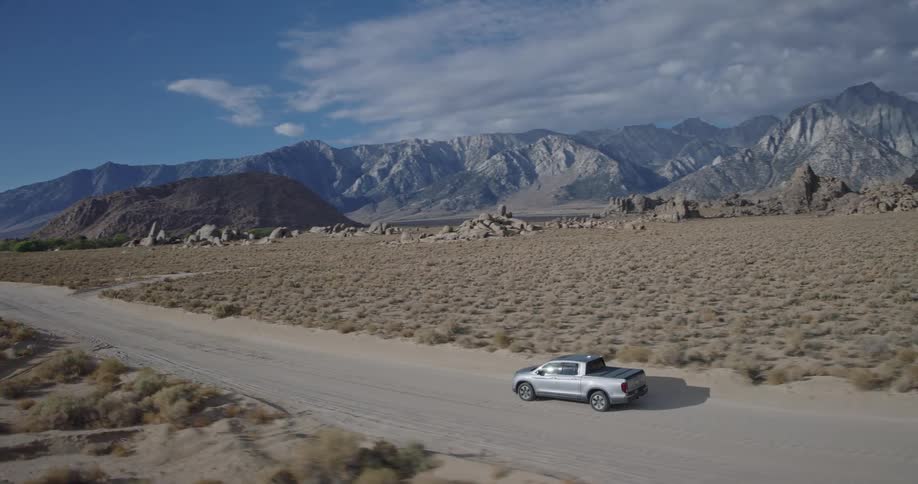 Silver pickup truck driving on dirt road in desert landscape with mountains in the background
