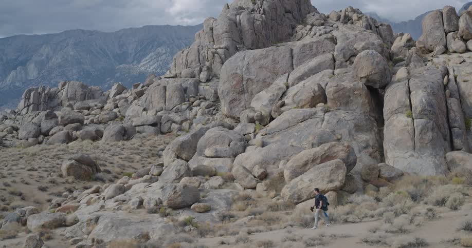 A man hikes across a rocky landscape located near a mountain range