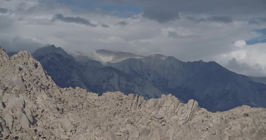 Jagged rock formations in the foreground with forested mountains and cloudy sky in the background